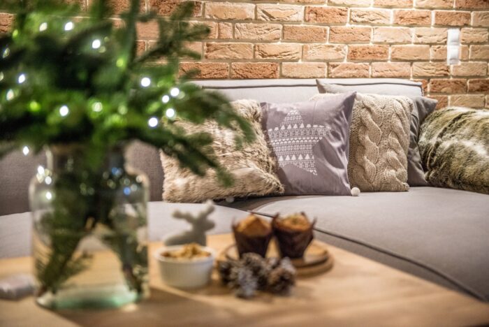 Sofa przyozdobiona kilkoma poduszkami zachęca do odpoczynku. Dzięki ciepłym dodatkom salon zyskuje na przytulności.