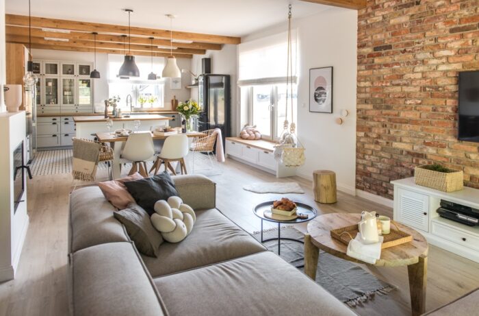 Szara sofa i czerwone cegły na ścianie kontrastują ze sobą, ale razem się uzupełniają. W salonie jest dużo dodatków,...
