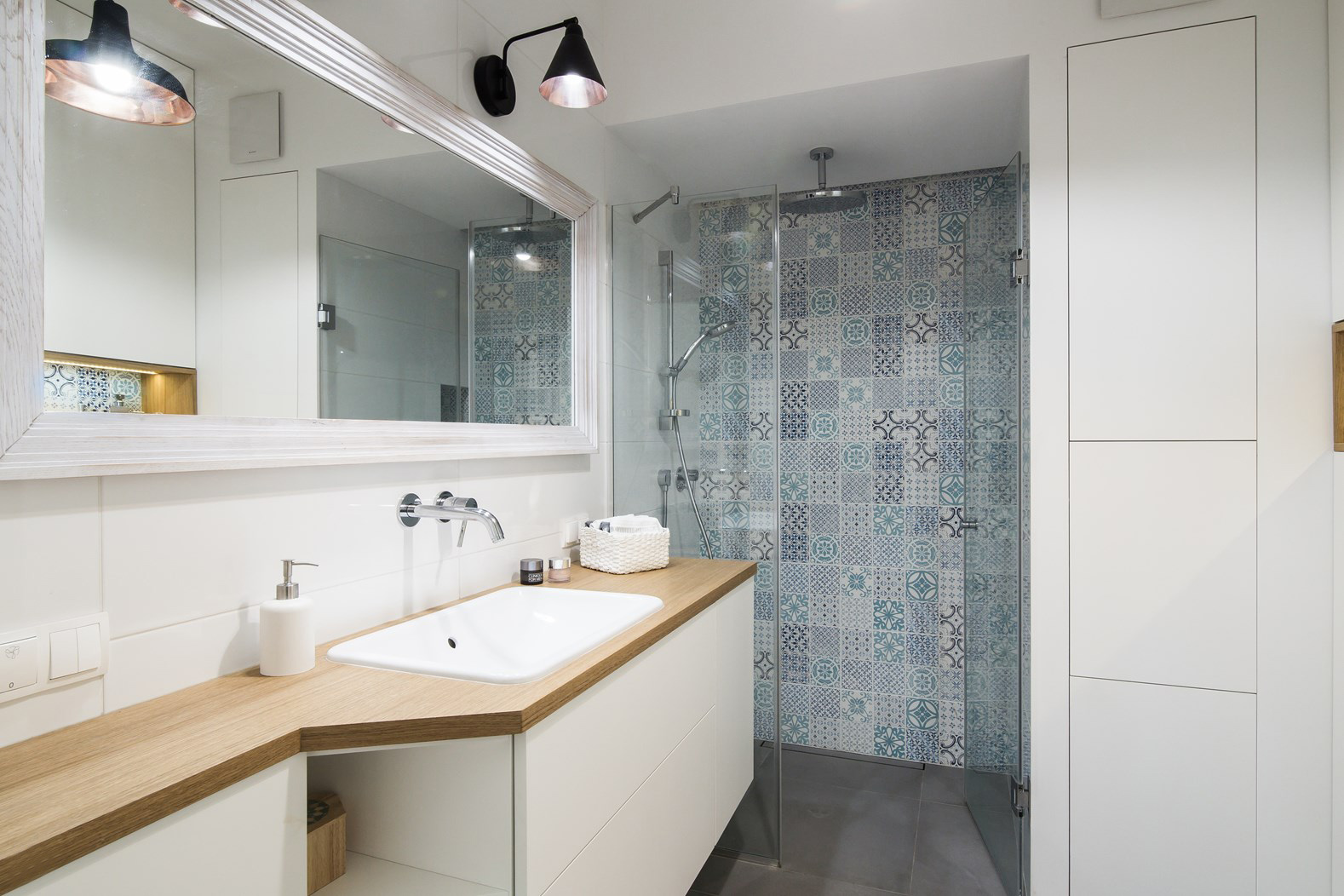 Aranżacja całkiem przestronnej łazienki w stylu skandynawskim, gdzie dominuje biel i drewno. Wzorzysta ściana w części...