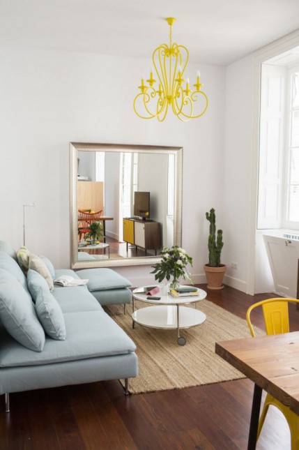 niebieska sofa modułowa z ikea,niebieski narożnik nowoczesne narożniki w jasnoniebieskim kolorze,żółty żyrandol,okrągły stolik na kółkach,kwadratowe duże lustro w salonie,arranzacja salonu w stylu skandynawskim,dywan z naturalnych włókien,dywan tkany na płasko,kawowe stoliki na kółkach,biały stolik okragły na kółkach,metalowe stoliki z białym okągłym blatem,meble z ikei,meble z ikea