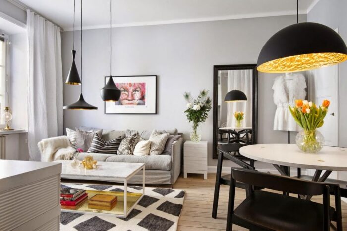 szare ściany w mieszkaniu,szare kolory scian w salonie,czarne lustro prostokatne na scianie w sslonie,czarne lampy wiszace,szara sofa z graficznymi poduszkami,salon otwarty z kuchnią,małe mieszkanie w otwartej zabudowie,kawalerka,małe mieszkanie dla singla,jak urzadzić mini mieszkanie,kawalerka w stonowanych barwach,aneks kuchenny przy salonie,pomysł na małe mieszkanie,szarobiałe wnętrza,czarne dodatki w małym mieszkaniu,czarne krzesła przy bialym stole,czarne metalowe lampy wiszace,dywan biało-szary w karo