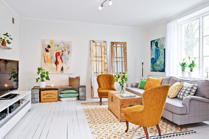 aranżacja salonu w słonecznych kolorach,żółte fotele,żółte dodatki we wnętrzach,skandynawski salon z detalami w stylu vintage,drzwi w stylu shabby ,drewniane skrzynki,biało-żółty dywan z ikei,fufer drewniany,skrzynia drewniana w roli stolika w salonbie,nowoczesne akwarele,biała sofa na kółkach,modne kanapy na kółkach,biała komoda TV,ozdobne poiduszki,dekoracyjne poduszki do salonu
